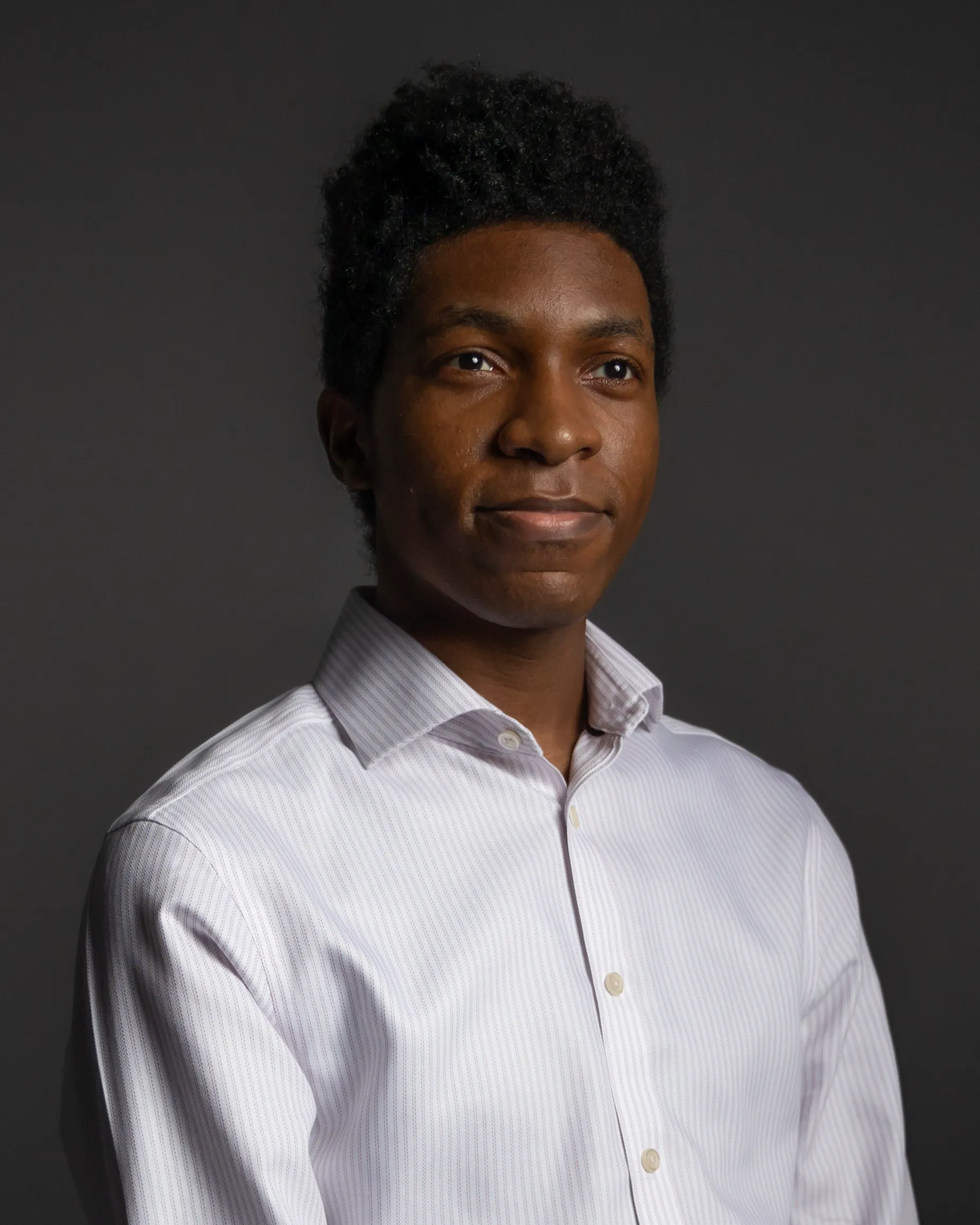 Headshot of Nick in a white and light pink striped dress shirt.